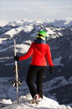 Female skier with ski helmet stands with ski at the ski slope over the valley