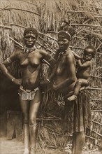 Two African women with a small child on their back in front of their hut