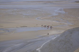 Hikers in mudflat at low tide in Mont Saint Michel