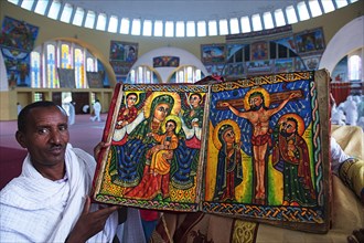 Priest shows hand-painted Bible with Mary and Jesus and Crucifixion Jesus