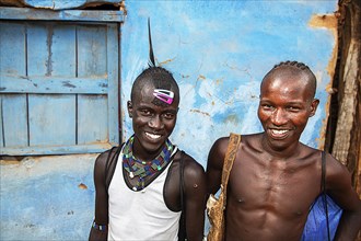 Laughing young men of the Hamer ethnic group with colorful hair clips and pearl jewelry
