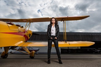 Young woman with leather jacket poses with yellow double-decker aviator