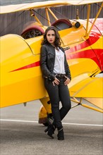 Young woman with leather jacket poses with yellow double-decker aviator