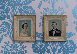 Pictures of Queen Elizabeth II and Prince Philip on wall with floral wallpaper