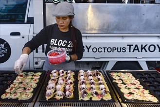 Woman sells baby octopus from grill at a food stall