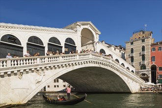 Tourists on Rialto bridge over Grand canal with traditional gondola