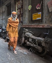 Hindu priest walks pass an abandoned motorcycle in the narrow streets