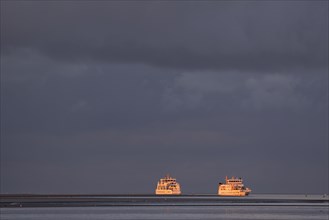 Two ferries meet in the waterway of Norderney in the evening light with dark clouds
