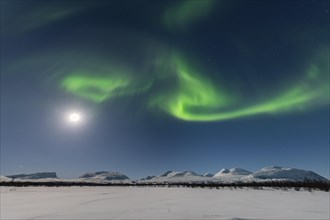 Northern Lights (Aurora Borealis) at full moon over snow-covered mountains