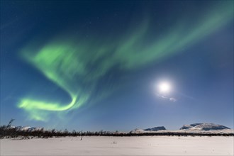 Northern Lights (Aurora Borealis) at full moon over snow-covered mountains