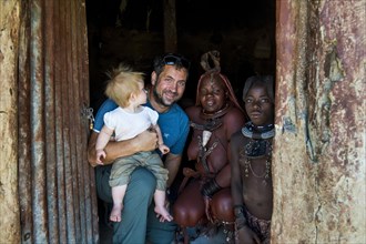 White tourist with his baby in a Himba village with Himba people