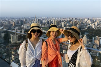 Three young Chinese tourists with hats on the viewing platform of the Maha Nakhon Tower