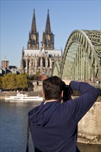 A man photographs Cologne Cathedral with the Hohenzollern Bridge