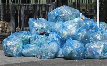 Full light blue garbage bags with plastic garbage on one heap