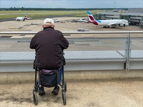 Disabled wheelchair user sits at the airport with a view of the tarmac