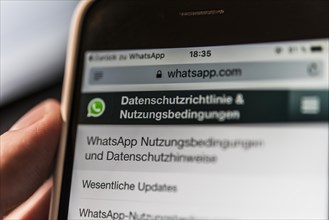Hand holding iPhone displaying WhatsApp terms of service and privacy policy
