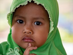 Little Indonesian girl with headscarf looks thoughtful