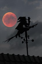 Blood moon over the roof of a house with weather vane with weather witch