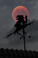Blood moon over the roof of a house with weather vane with weather witch