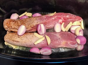 Loin of pork with shallots and garlic in a roaster for cooking