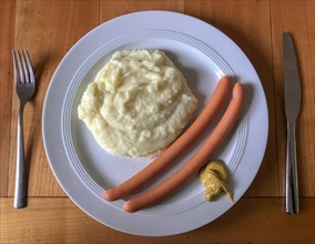 Sausage with mashed potatoes and mustard on plate with cutlery