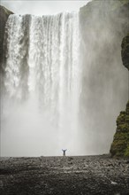 Person with arms outstretched in front of waterfall
