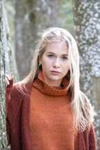 Young girl with long blond hair leaning on a tree