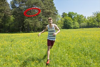 Young man chasing frisbee in meadow