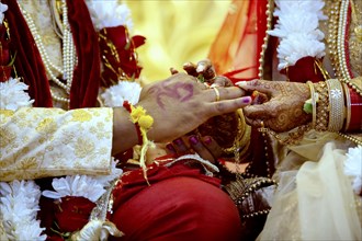 Bride with bridal jewelry and henna decoration on her hand attaches ring to the grooms finger at traditional religious ceremony at a Hindu wedding