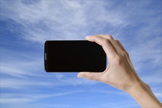 Hand holding smartphone with black screen in front of blue sky