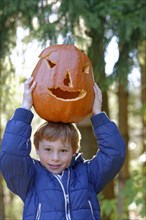 Boy balancing a Halloween pumpkin on his head in autumn