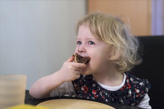 Little blonde girl biting into a bun with chocolate spread
