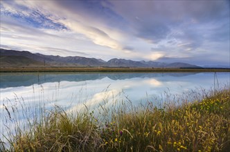 Mountains of the Southern Alps reflected in Tekapo Canal with cloudy sky