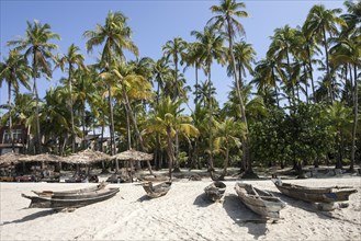 Beach with old parasols and fishing boats under palm trees in Ngapali Beach