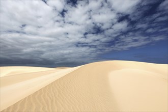 Sand dunes under blue sky with clouds