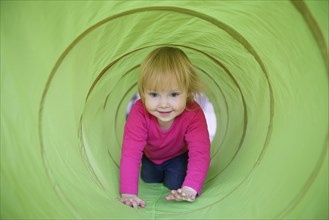Little girl with pink shirt crawling through green playing tunnel