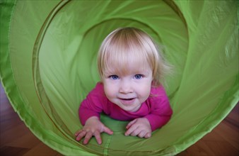 Little girl with pink shirt crawling through green playing tunnel