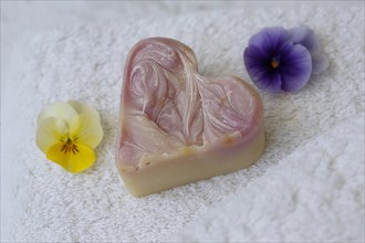 Soap in heart shape on terry towel with flowers of horned violets