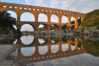 Roman aqueduct Pont du Gard reflected in the Gardon river in the evening