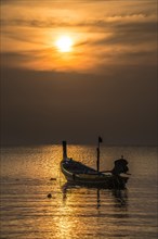 Long-tail boat in sea at sunset