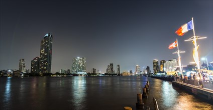 River promenade in the evening with a Ferris wheel and the skyline on the river Mae Nam Chao Phraya