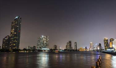 River promenade in the evening with a Ferris wheel and the skyline on the river Mae Nam Chao Phraya