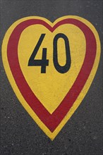 Red-yellow speed limit sign "40" in heart shape on an asphalt road