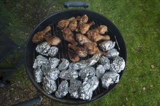 Baked potatoes and chicken legs on grill