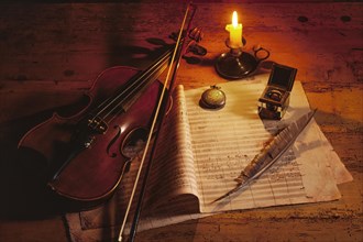Violin with music sheet and quill by candlelight