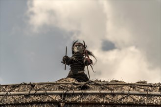 Figure on the roof of a thatched wooden house