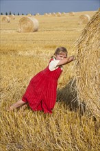 Little girl tries to move away a straw bale on a stubble field