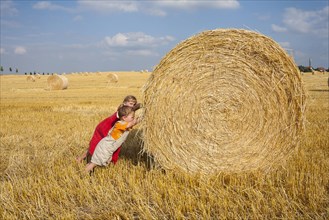 Little girl and boy trying to move away a straw bale on a stubble field