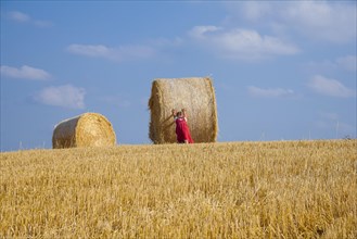 Little girl tries to move away a straw bale on a stubble field