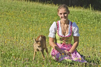 Woman in dirndl with a tame fawn in a flower meadow